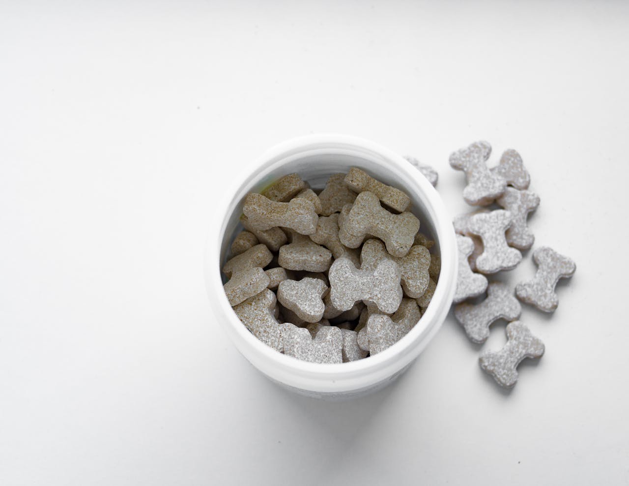 who-we-are Close-up of bone-shaped dog treats in a white container on a white surface.